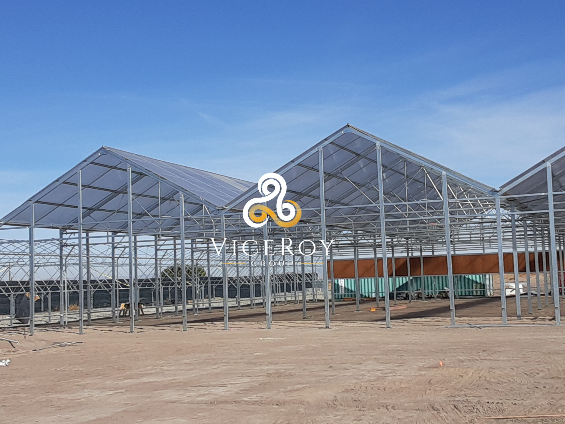 Greenhouse steel framework during construction, with partial polycarbonate cladding under a blue sky