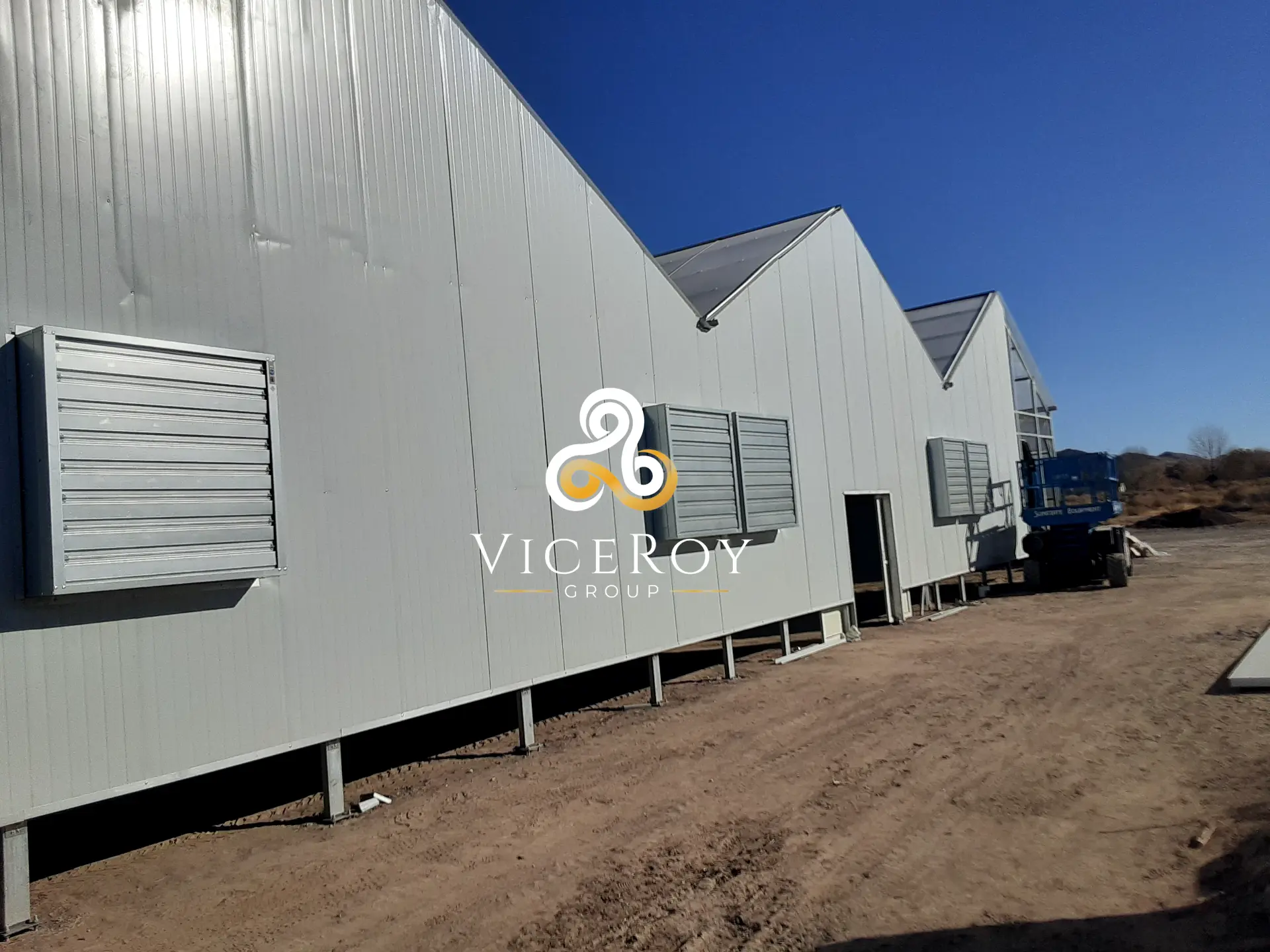 Greenhouse exterior showing the structural configuration and ventilation equipment, with a scissor lift alongside
