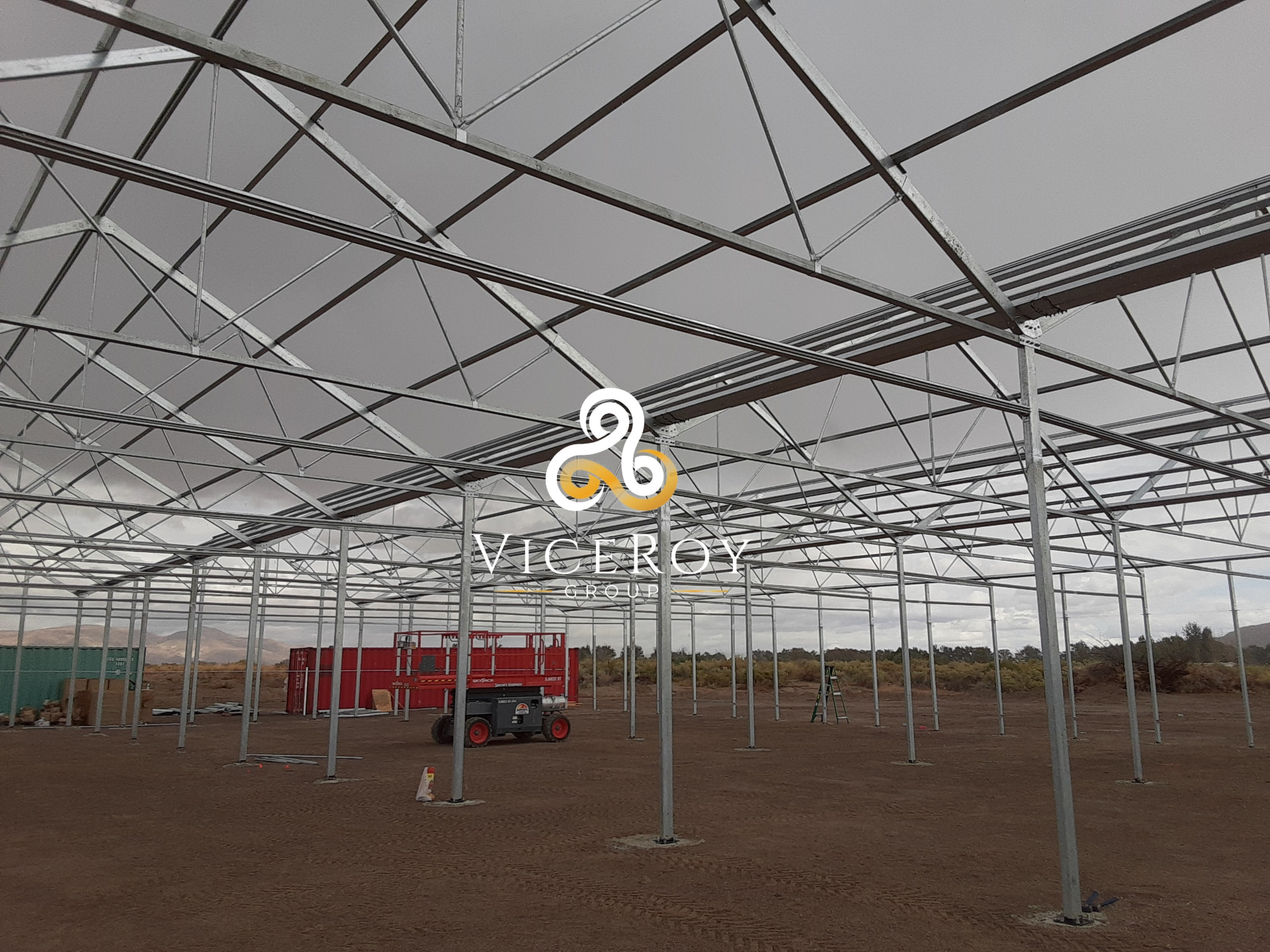 On-site installation of the greenhouse structural framework, with a scissor lift inside the open steel structure